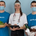 Three volunteers promoting eco-friendly practices with plants and recycling materials.