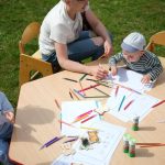 Children and parents engaging in outdoor art and craft activities with colored pencils.